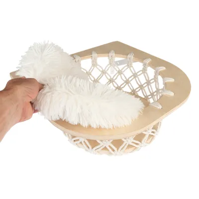 Hand legt ein weisses, flauschiges Kissen in einen Hängesitz aus Holz und Seilnetz.