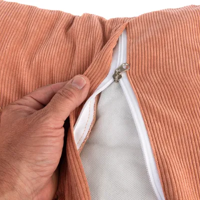 Povečava oranžne prevleke za blazino z zadrgo, odprta, prikazuje belo notranjo tkanino. Roka drži prevleko za prikaz.