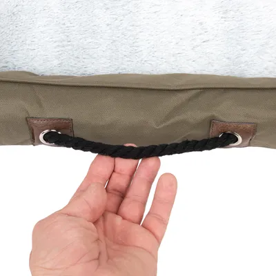 Detailaufnahme eines braunen Tragegriffs aus Seil mit Metallösen an einem khakifarbenen Stoff, gehalten von einer Hand.