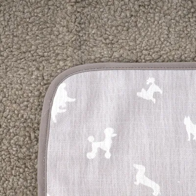 Coin d’un tapis en tissu gris à motifs silhouettes de chiens blancs, bordure grise visible, posé sur une moquette beige à texture bouclée.