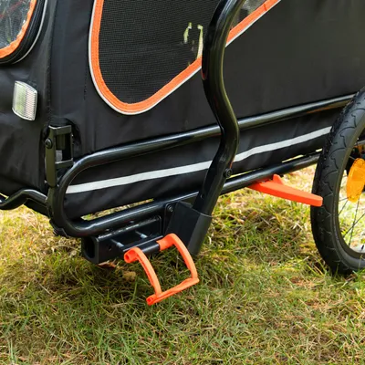 Närbild av en cykelvagn med svart tyg, orange detaljer och reflexremsor. Synlig koppling för fastsättning på cykel.