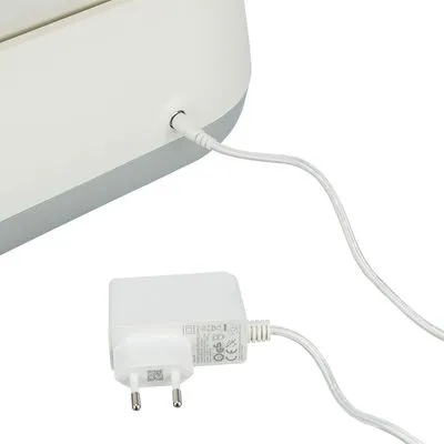 Wit netsnoer met stekker aangesloten op een wit elektrisch apparaat. Adapter met CE-markering en technische specificaties zichtbaar op de behuizing.