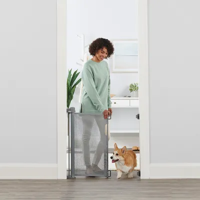 Barrière de sécurité en maille grise installée dans une porte, avec un chien de petite taille passant à côté d’une personne debout derrière la barrière.