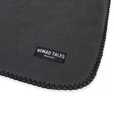 Graue Decke mit schwarzem Label 'Nomad Tales München' und dekorativer Naht an den Rändern.