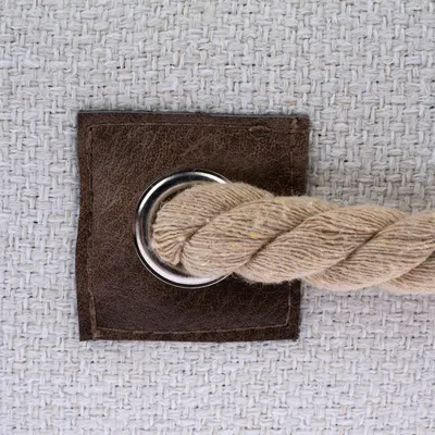Närbild av ett beige rep, fäst med en metallögla på en brun läderplatta, monterad på ett vitt tyg med vävd struktur.