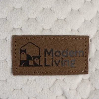 Modern Living. Logo auf braunem Etikett mit Haus- und Tiermotiven, genäht auf weissem, gestepptem Stoff.