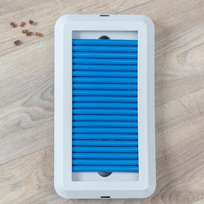 Leksak med blåa gummirör i vit ram på trägolv. Små godisbitar bredvid.