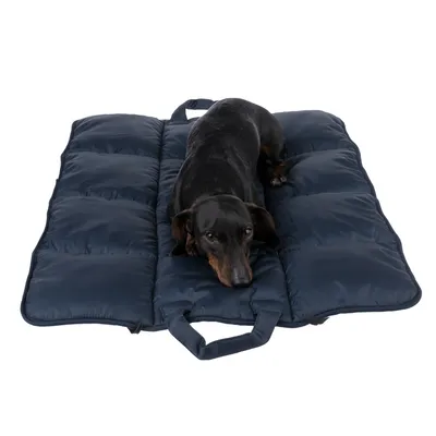 Ciemnoniebieska, pikowana mata dla psa z uchwytami do przenoszenia. Pies leży na macie.