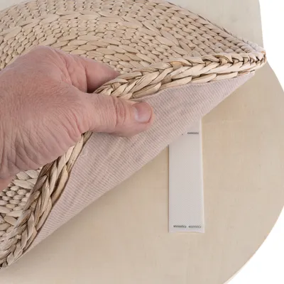 Hand lifts a braided mat with hook-and-loop fastener from a wooden surface, showing removable function.
