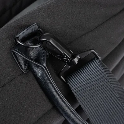 Detailaufnahme eines schwarzen Karabinerhakens aus Metall, befestigt an einem robusten Nylonband und einer Lederhalterung.