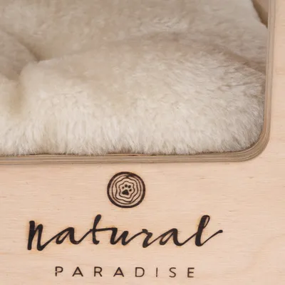 Natural Paradise márkanév fa felületen, felette puha, krémszínű szövet látható.