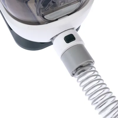 Close-up view of a white and grey device with a transparent tube and green push button. Functional elements visible.