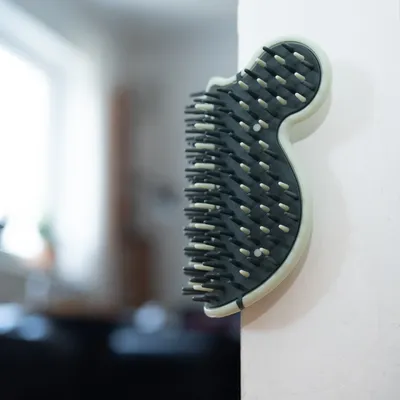 Black and white wall brush with plastic bristles, mounted on a white wall. Suitable for coat care by rubbing.