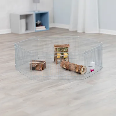 Metallgehege mit Gitterwänden, ausgestattet mit Holzspielzeug, einem Häuschen und einer Trinkflasche. Geeignet für Innenräume auf hellem Laminatboden.
