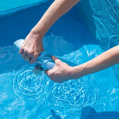 Hände wringen ein blaues Reinigungstuch über einem Pool aus, Wasser tropft ins Becken.