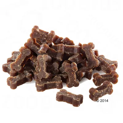 Petites friandises brunes en forme d’os, empilées sur fond blanc. Aucun emballage ou marque visible.