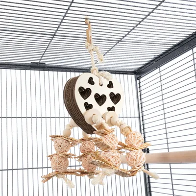Jouet suspendu en forme de cœur avec motifs cœurs découpés, boules et bâtonnets en bois et corde, accroché dans une cage pour oiseaux ou petits animaux.