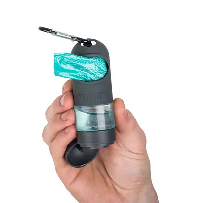 Hand houdt grijze KONG dispenser met karabijnhaak, geïntegreerd vak voor hondenpoepzakjes en transparante watercontainer.