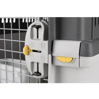 Detaljvy av ett låssystem med gul skjutreglage och "Lock"-märkning på en transportbur med galler.