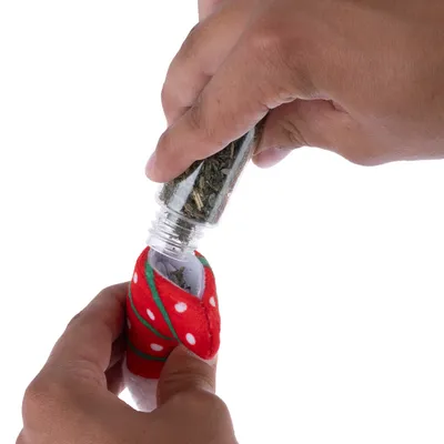 Hand füllt Kräuter aus einer Flasche in ein rotes Stoffspielzeug mit weissen Punkten.