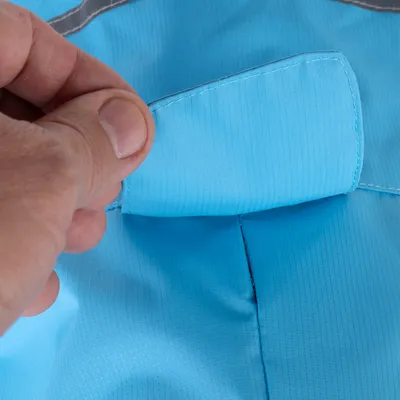 Gros plan sur une main soulevant un rabat en tissu bleu avec couture visible, montrant le détail de la fermeture d’un vêtement ou accessoire pour animal.