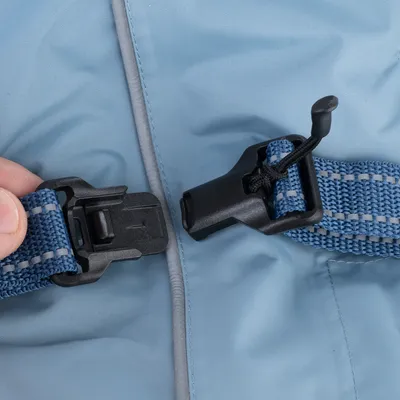 Gros plan sur une fermeture à clip en plastique noir avec sangle bleue et surpiqûres grises, tenue par une main, sur un tissu bleu clair matelassé.