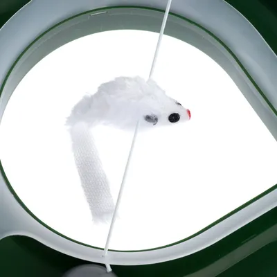 Juguete blanco en forma de ratón con ojos negros y nariz roja, sujeto a una cuerda en un marco verde.