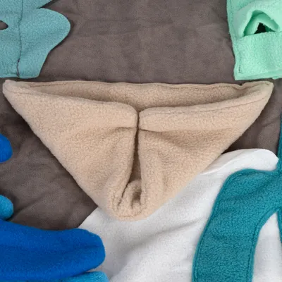 Beige fleece fabric in triangular shape, surrounded by colourful fabric pieces in blue, white and green on grey background.