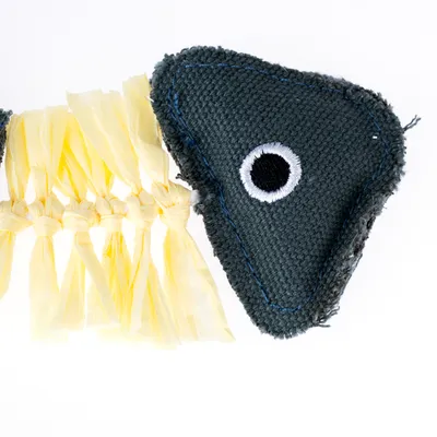Jouet en forme de poisson avec tête en tissu bleu foncé et œil brodé, corps composé de lanières jaunes tressées. Matériaux visibles : tissu et fibres.