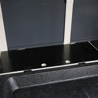Placa de madera negra con dos huecos redondos, integrada en una carcasa gris. Vista detallada del interior.