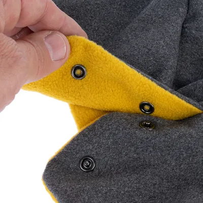 Gros plan sur une main tenant un tissu gris et jaune avec boutons-pression visibles, matière polaire. Montre le système de fermeture du produit.