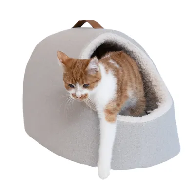 Kattenhuis van grijze stof met zachte, witte voering en handvat bovenop. Kat steekt een poot uit de ingang.