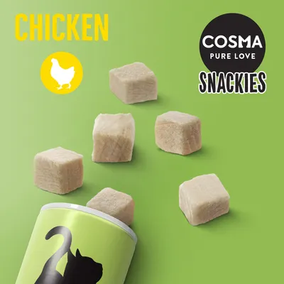 COSMA PURE LOVE SNACKIES CHICKEN, kostky pamlsků s kuřecím masem vysypané z obalu se siluetou kočky na zeleném pozadí