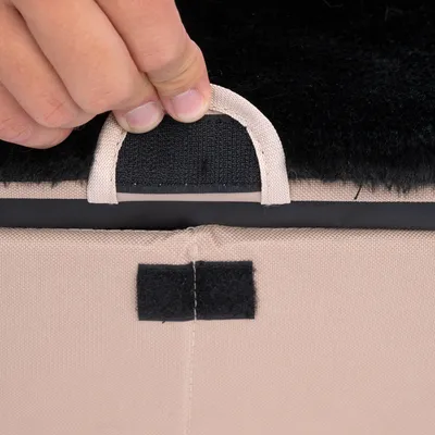 Nahaufnahme einer Hand, die eine Lasche mit Klettverschluss an einem beige-schwarzen Stoff hebt. Zeigt die Funktion des abnehmbaren Bezugs.