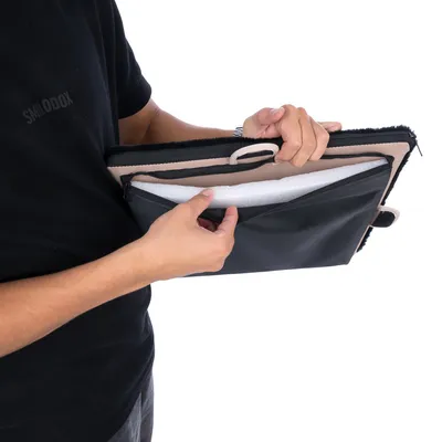 Person zeigt eine schwarze Tasche mit mehreren Fächern, darunter ein gepolstertes Fach und ein Reissverschlussfach.