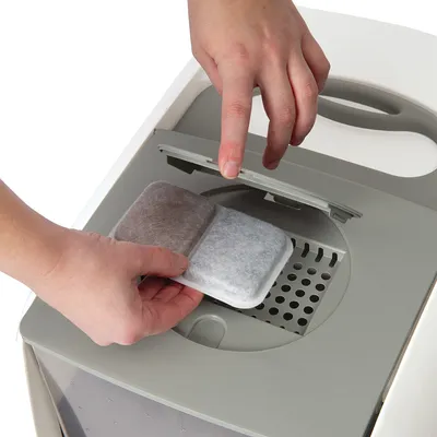 Main insérant un filtre rectangulaire à double compartiment dans le couvercle d’un bac gris clair avec poignée intégrée. Aucun texte visible.