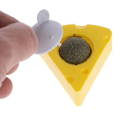 Gelbes dreieckiges Spielzeug mit herausnehmbarem Deckel, darunter ein grüner Ball aus gepresstem Material. Hand zeigt Öffnung des Deckels.
