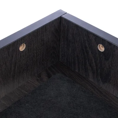 Angolo di un prodotto in legno nero con due fori rotondi e superficie in feltro nero.