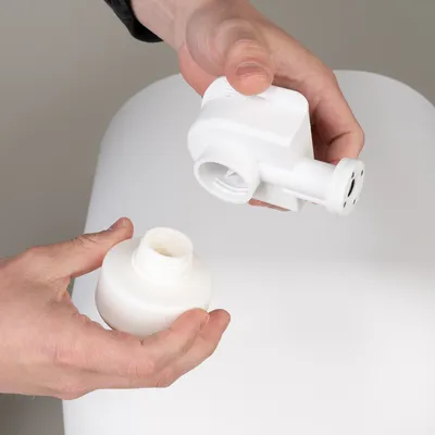 Hands showing the assembly of a white accessory part with screw cap, consisting of two parts.