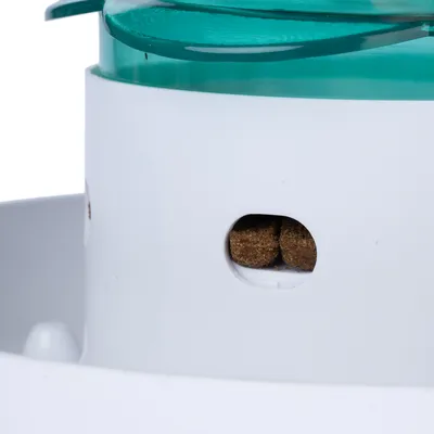 Nahaufnahme eines weissen Futterautomaten mit grünem Deckel. Sichtfenster zeigt braune Trockenfutterstücke im Inneren.