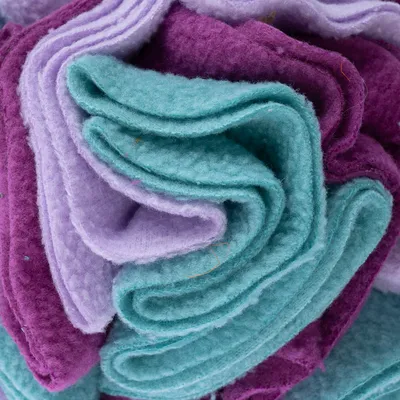 Nærbillede af foldet stof i lilla, lyse lilla og turkis, muligvis fleece.