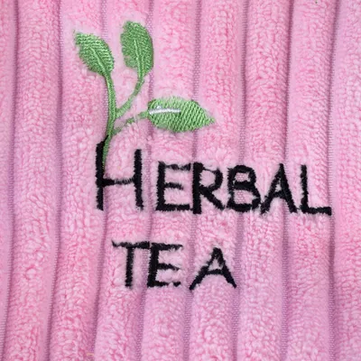 Stickerei mit grünem Blattmotiv und Text 'Herbal Tea' auf rosa Stoff.