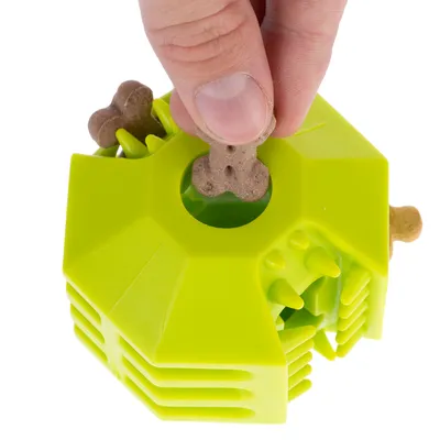 Una mano inserisce uno snack a forma di osso in un gioco verde con aperture e protuberanze.