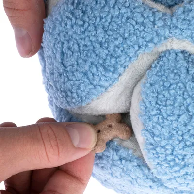 Hand stopt een hondenkoekje in een blauw pluchen speeltje met verborgen vak.