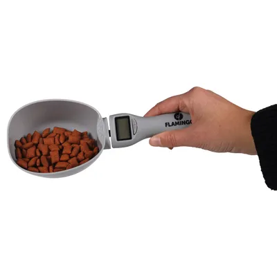 Hand holding grey measuring scoop with digital display, filled with brown kibbles. Flamingo brand visible on handle.