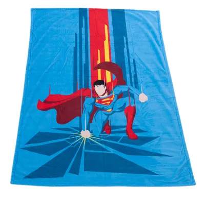Couverture bleue en tissu avec illustration de Superman, costume bleu et rouge, cape rouge, logo S jaune sur la poitrine, fond graphique bleu et rouge.