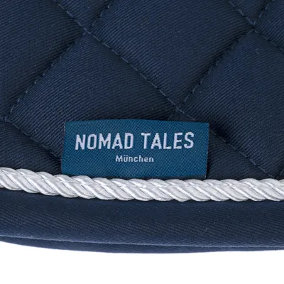 Nomad Tales München. Markenetikett auf dunkelblauem, gestepptem Stoff mit weisser Kordel.