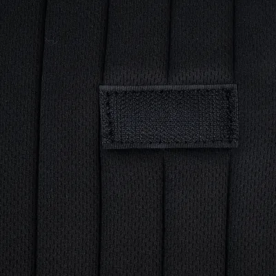 Nahaufnahme eines schwarzen Stoffmaterials mit einer rechteckigen, genähten Lasche. Struktur des Materials ist sichtbar.
