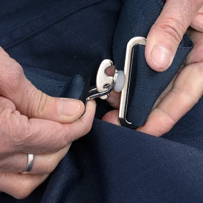 Close-up van een hand die een zilverkleurige metalen sluiting aan een donkerblauwe stof bevestigt.