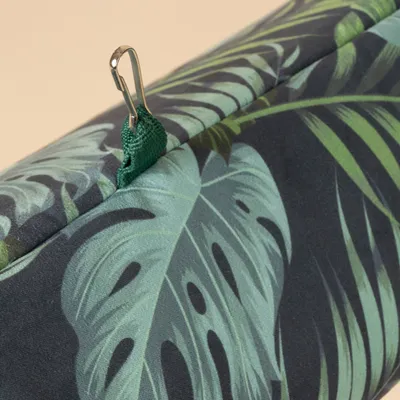 Primer plano de un estampado tropical en una tela con cinta de sujeción verde y mosquetón metálico.